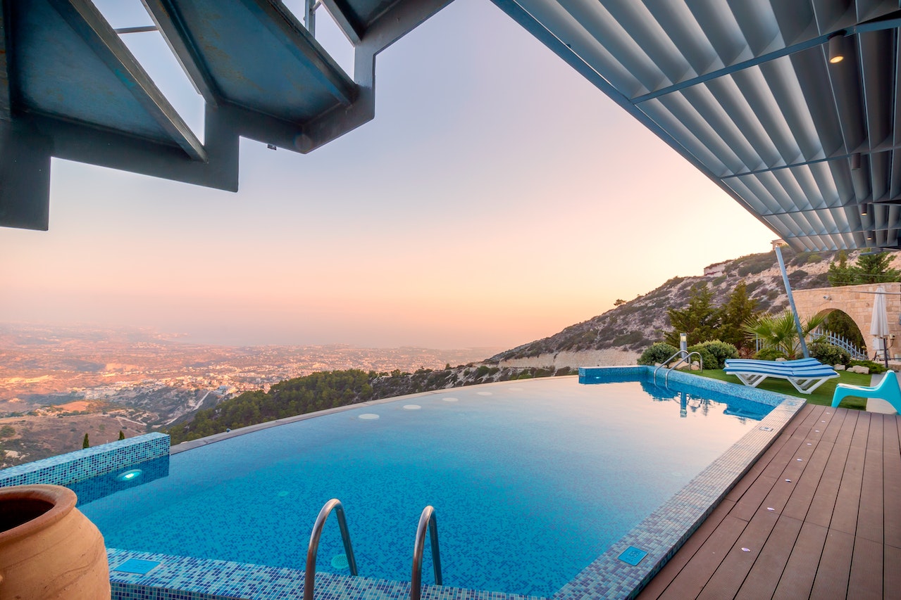 A beautiful pool on the edge of a home with a view of a city underneath it.