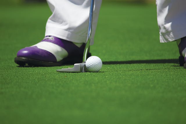 Close-up shot of a person in white and purple shoes playing golf