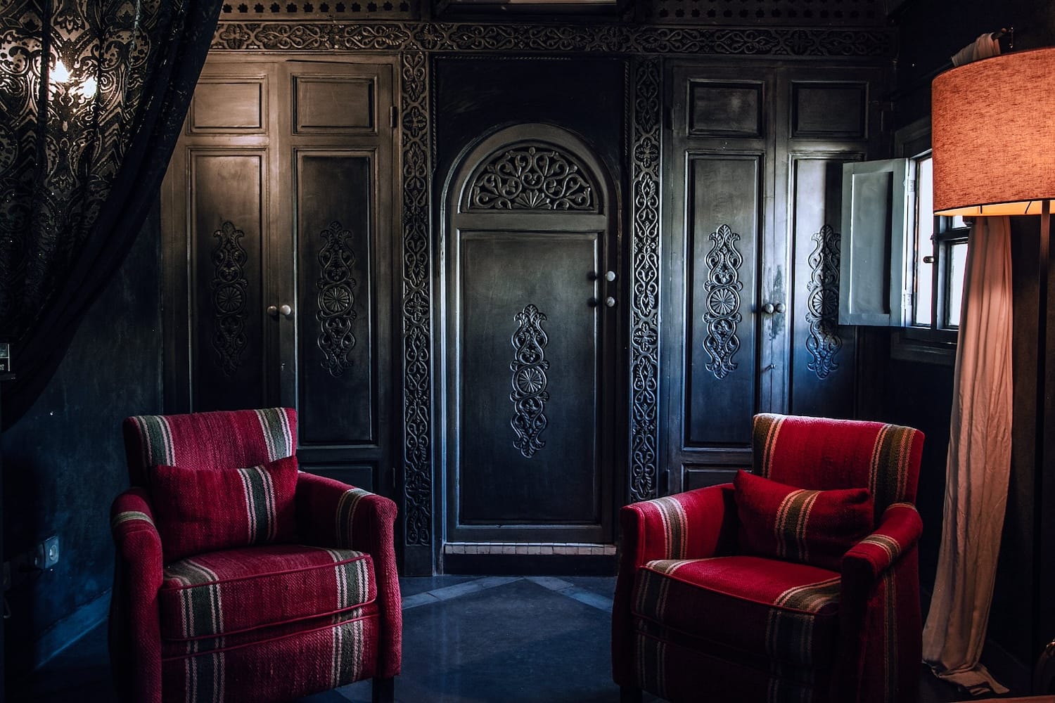 Black, ornate closet with red armchairs and a lamp