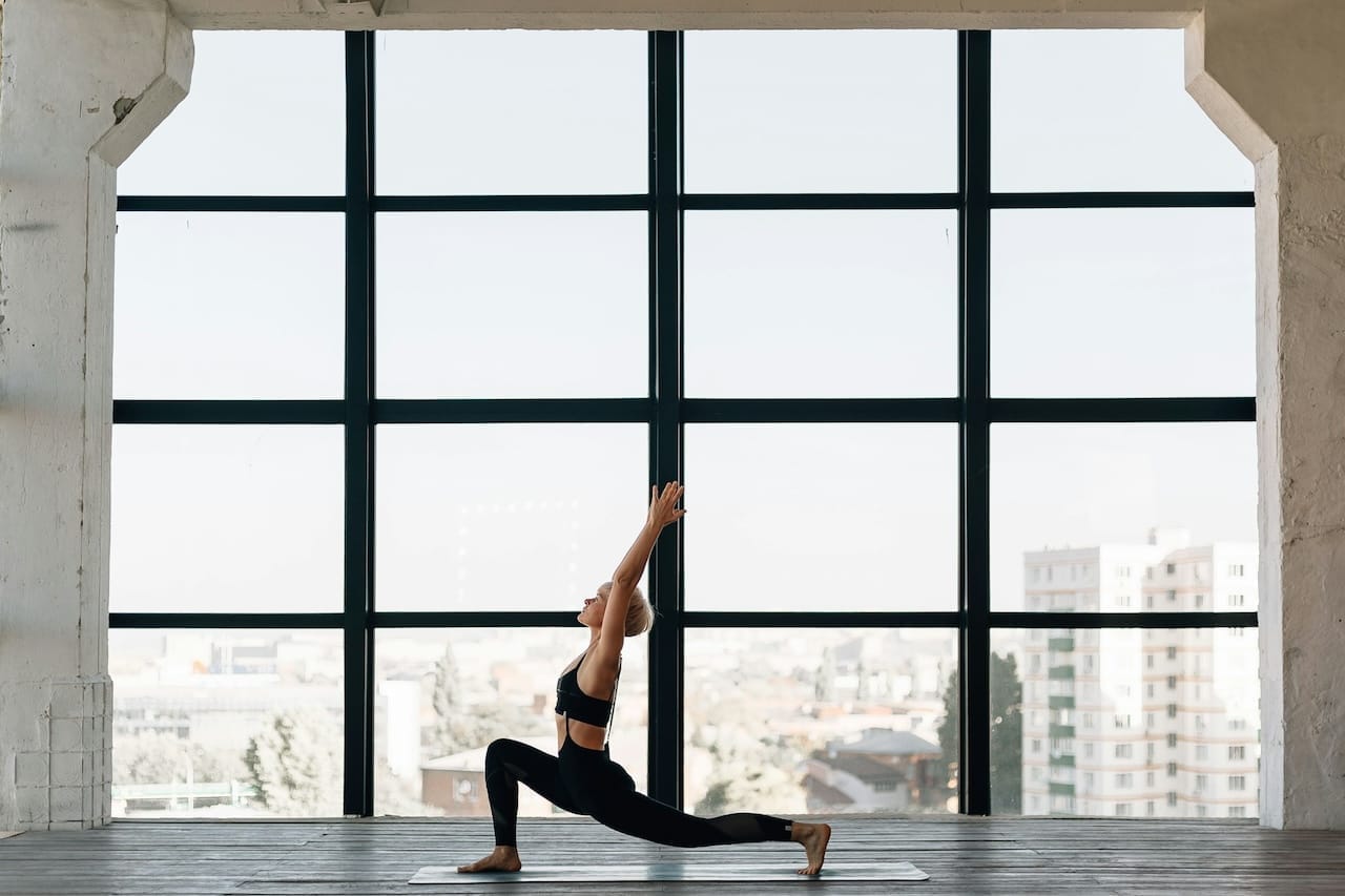 A woman in black doing yoga near the window
